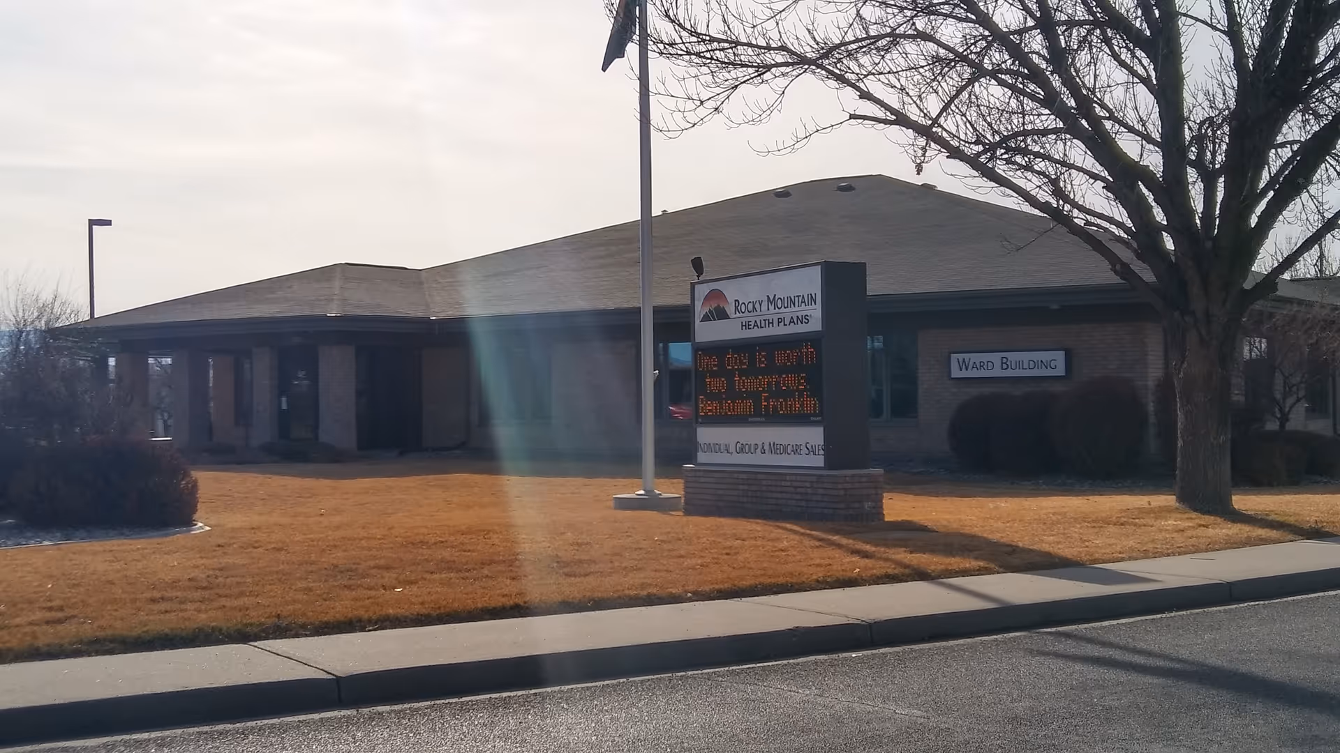 Exterior view of a brick facility with a Ward Building sign and bare lawn.