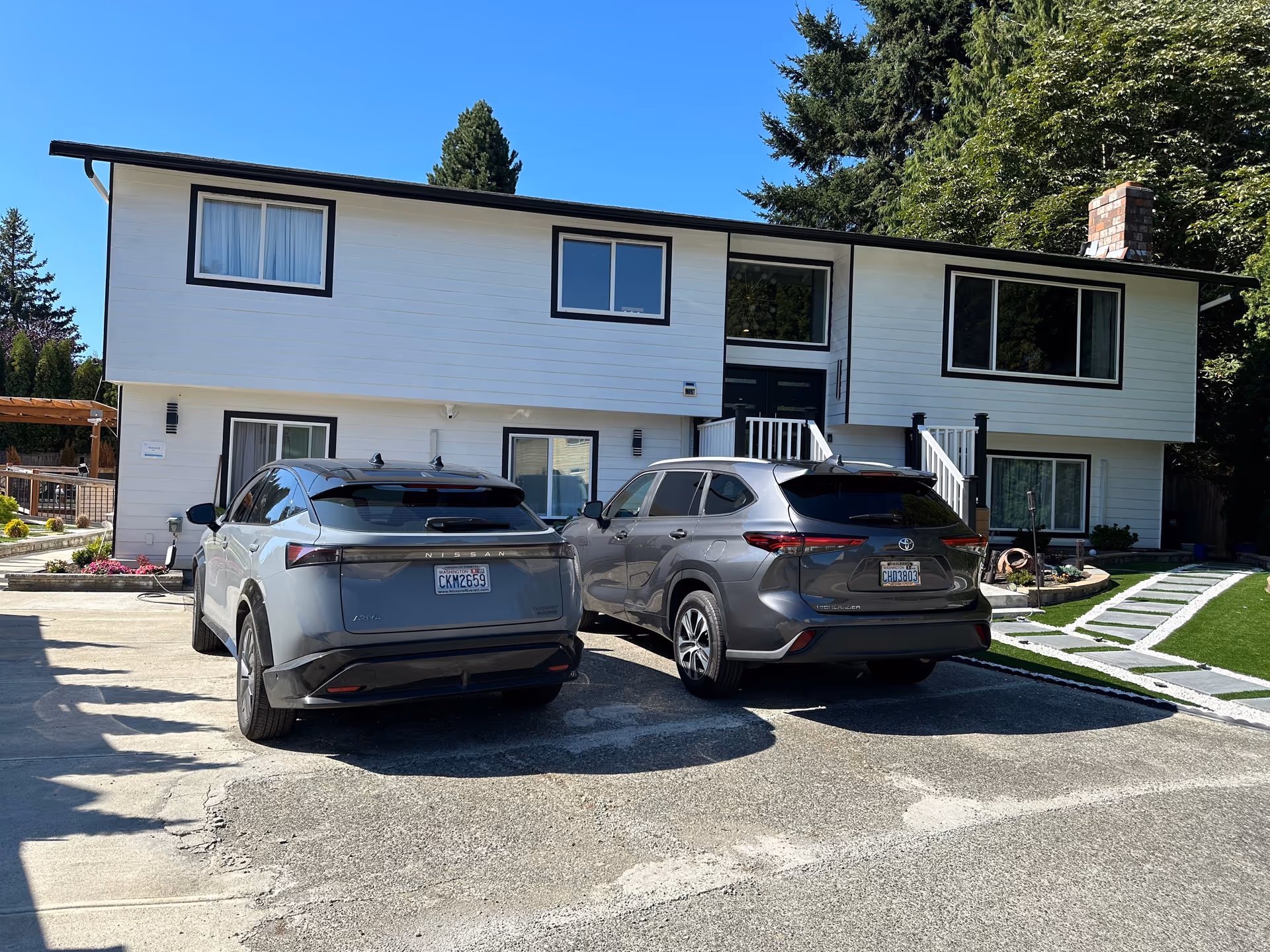 Two-story white building with black trim, stairs, and two parked cars in front