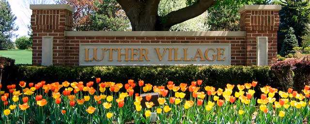 Exterior brick sign reading Luther Village with a tulip garden in front.