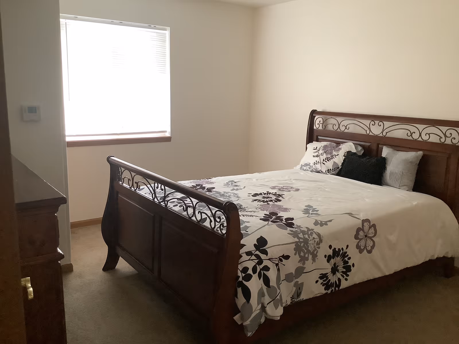 A bedroom with a large wooden bed, floral bedding, and a window.