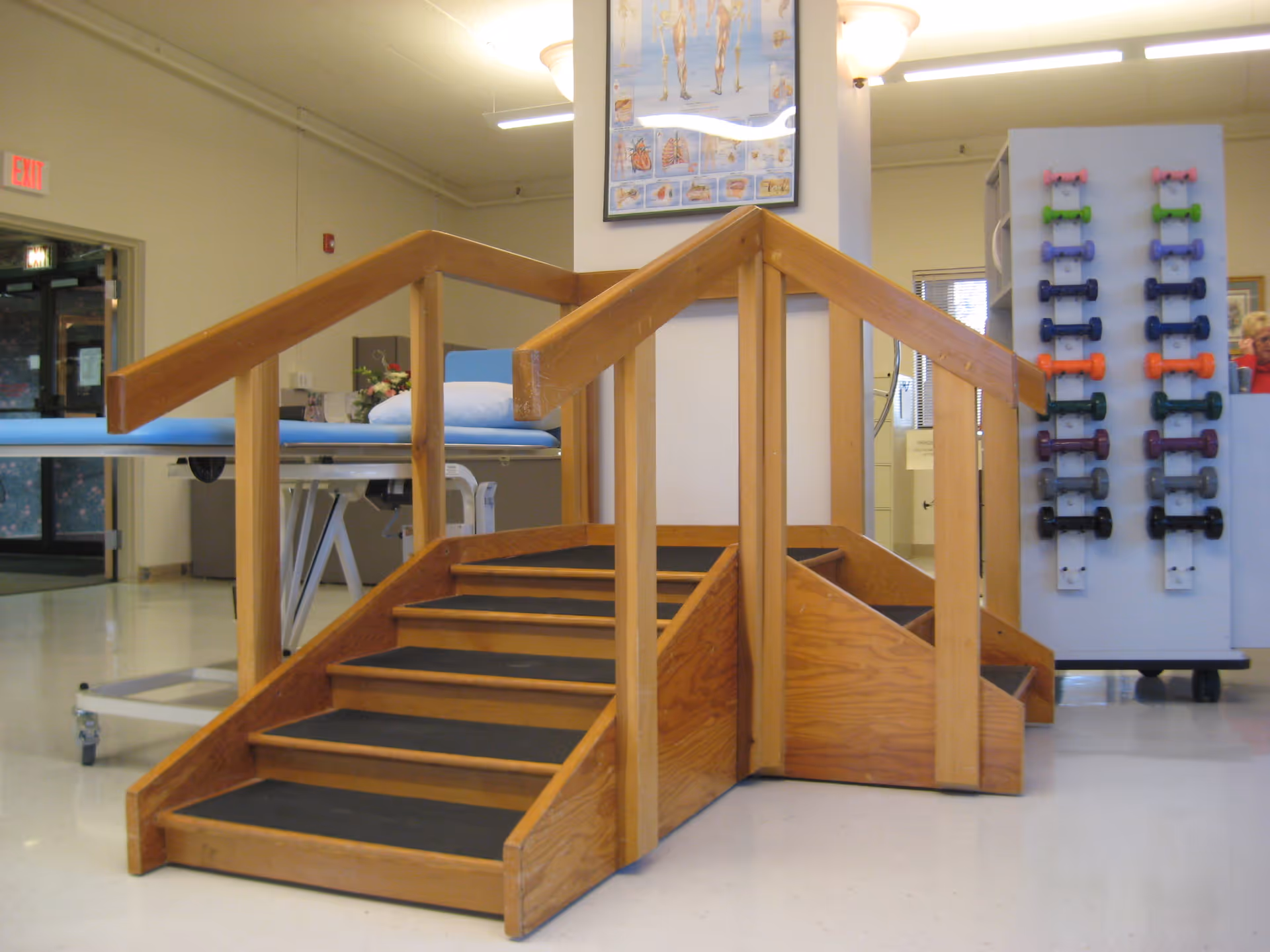 Wooden staircase with rails in a rehabilitation gym, surrounded by exercise equipment.