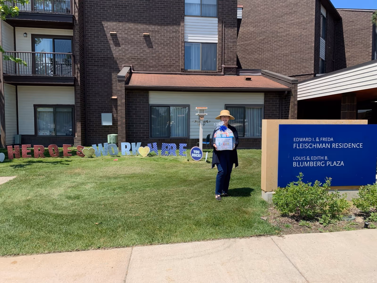 Person stands on a grassy lawn in front of a brick building and sign.