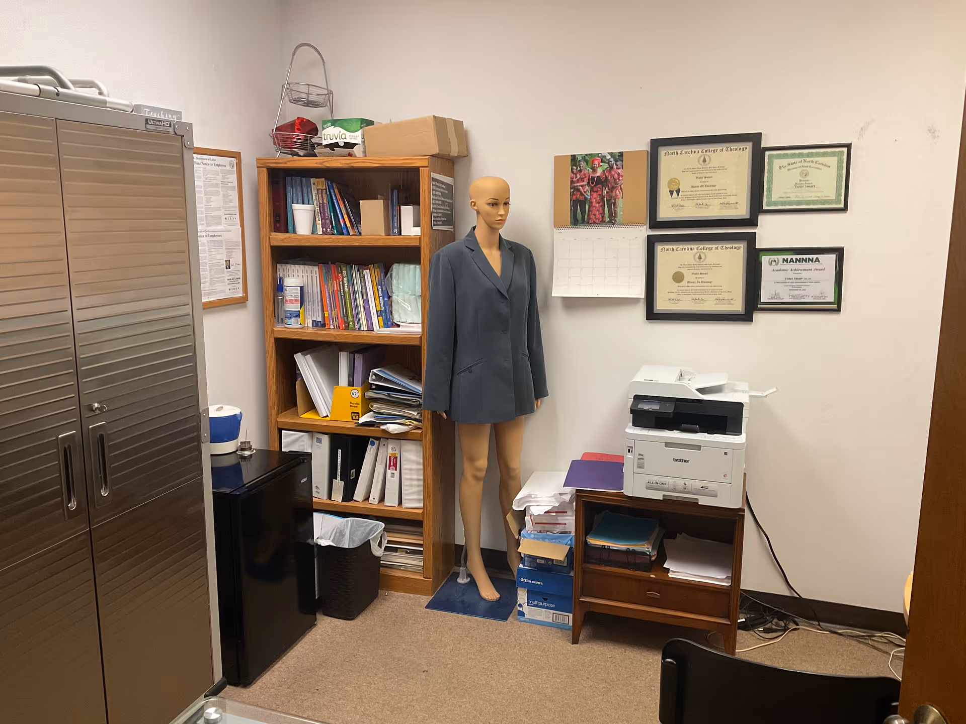 Office space with a mannequin, shelves, and a printer in a senior living facility.