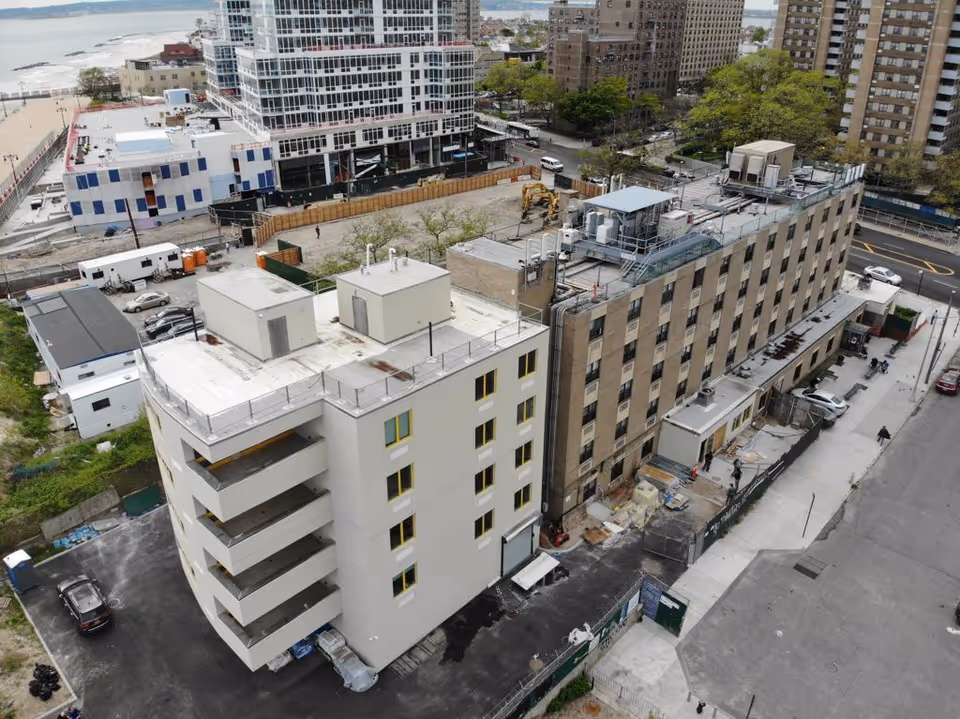 Aerial view of a multi-story senior living building and adjacent construction sites near the waterfront.
