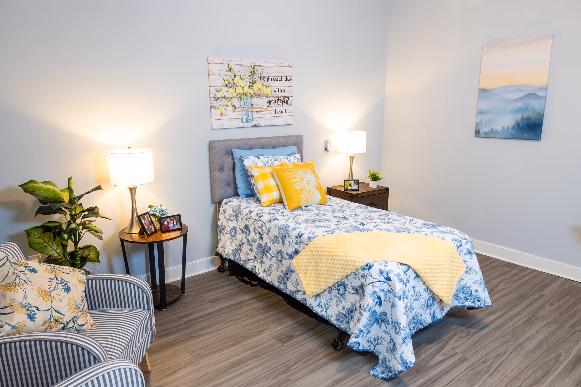 A cozy bedroom with a blue floral bedspread, yellow pillows, and bedside lamps.