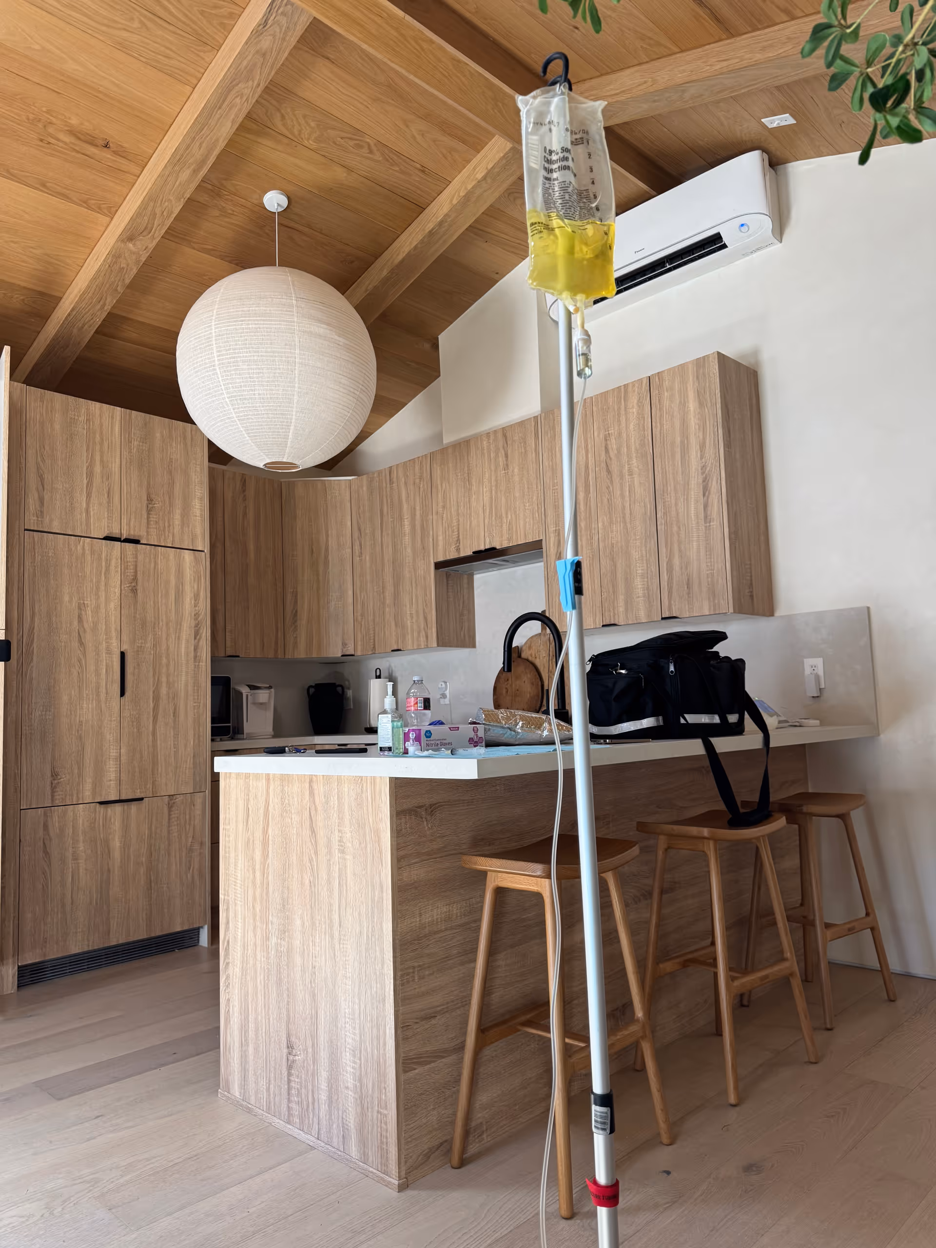 Modern wooden kitchen with island, stools, and an IV drip pole in foreground.