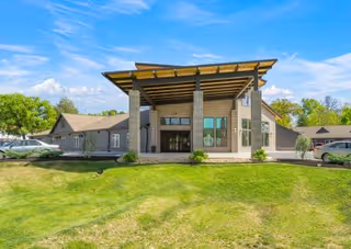 Modern senior living facility entrance with brick columns, glass doors, and a manicured lawn.