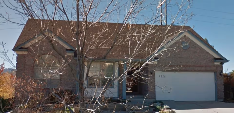 A brick, single-story home with a two-car garage and leafless trees in the front yard.