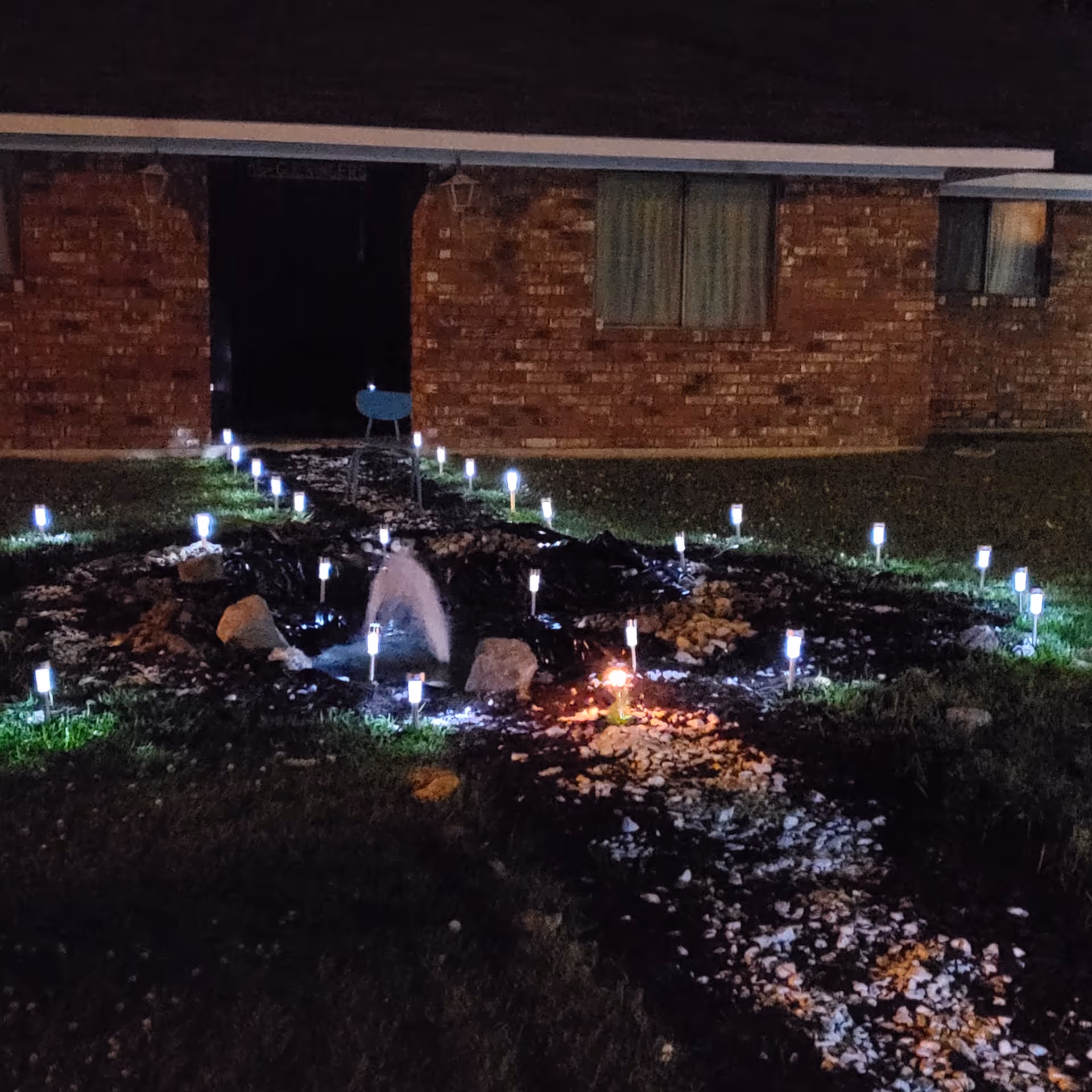 Night exterior of brick building with illuminated garden path and small fountain.