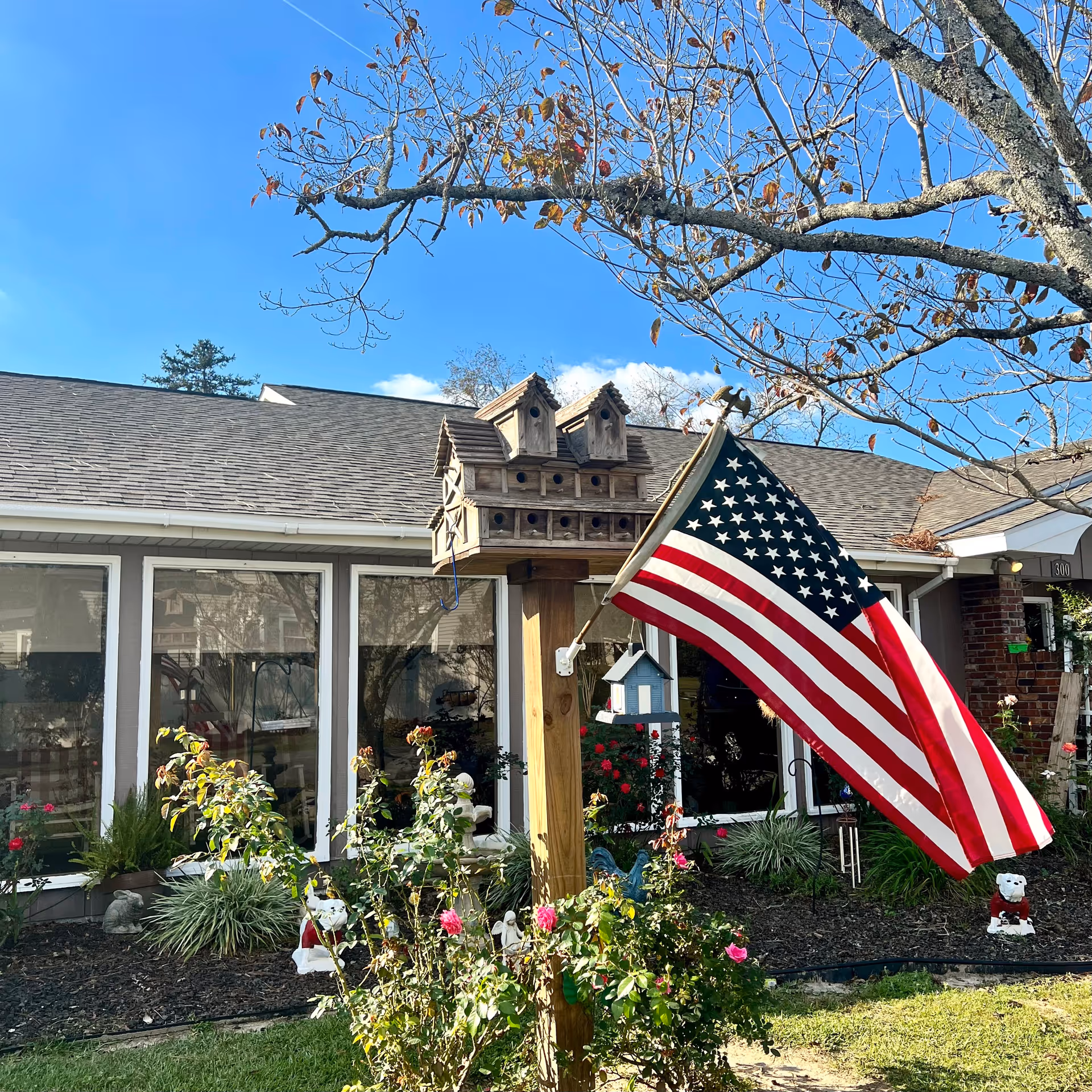 Front exterior of Magnolia Personal Care Home with flag, garden, and birdhouse.