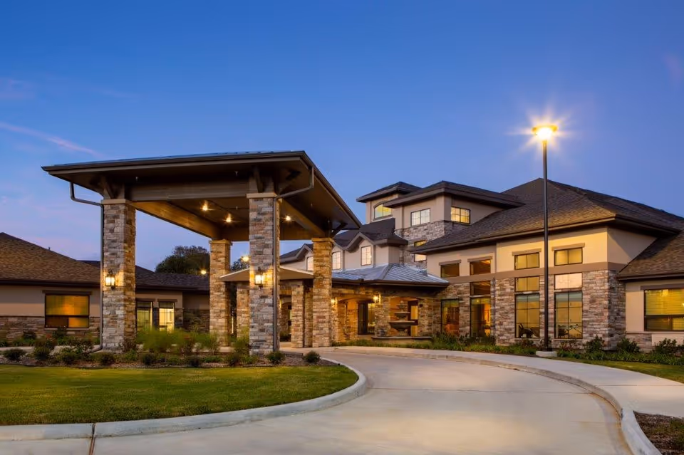 Exterior view of The Shores at Clear Lake senior living facility with driveway and lit entrance.