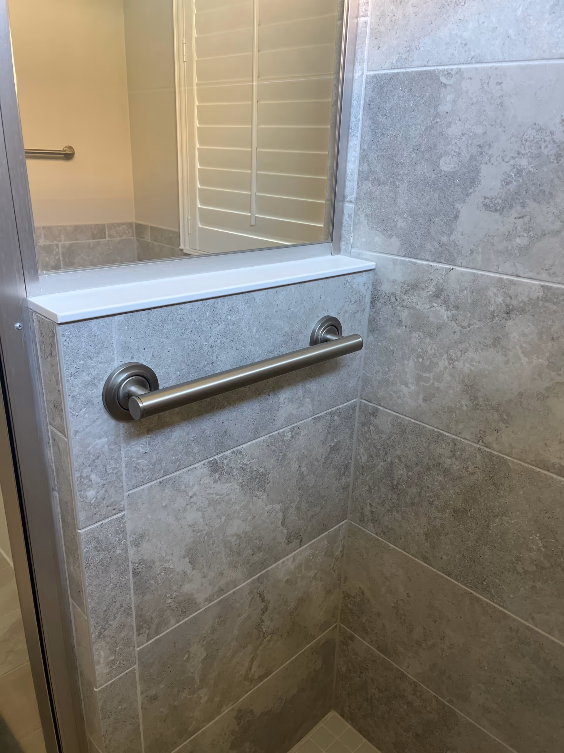Accessible bathroom with gray tiled walls, a mirror, and a stainless steel grab bar.