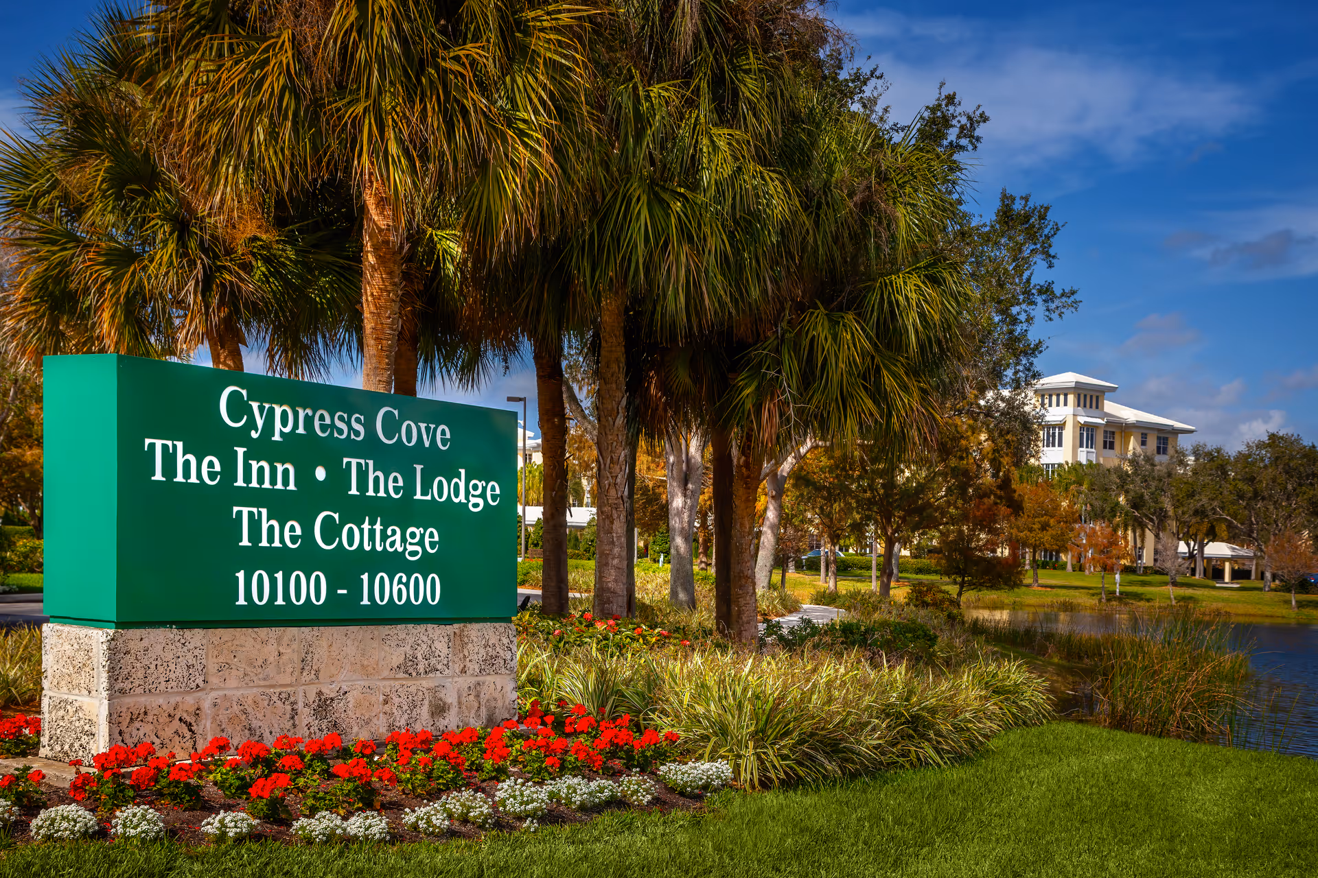 Cypress Cove sign with palm trees, landscaped garden, and a building in the background.