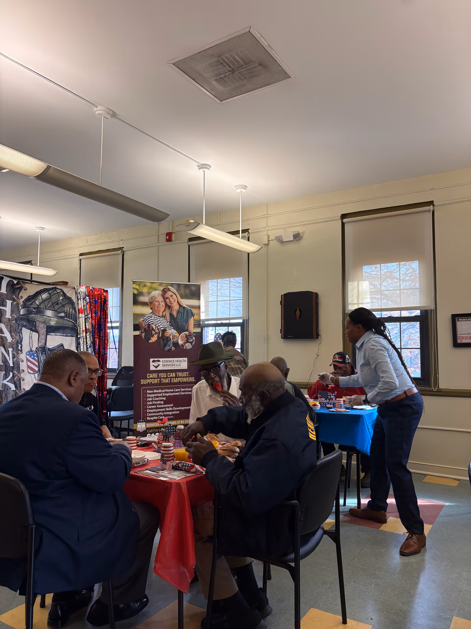 Residents and staff dine together in a communal dining room with a server assisting.