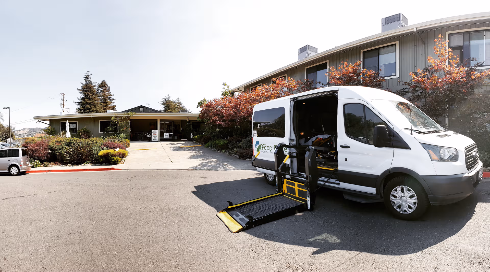 A white wheelchair van with a ramp parked at the front of a senior living building.