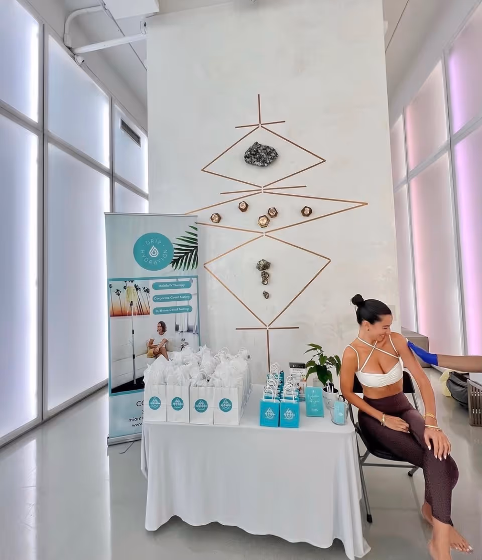 A promotional table with gift bags and a seated woman in a modern IV therapy clinic.