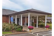 Front entrance of a brick senior living facility with a handicap sign and potted flowers.