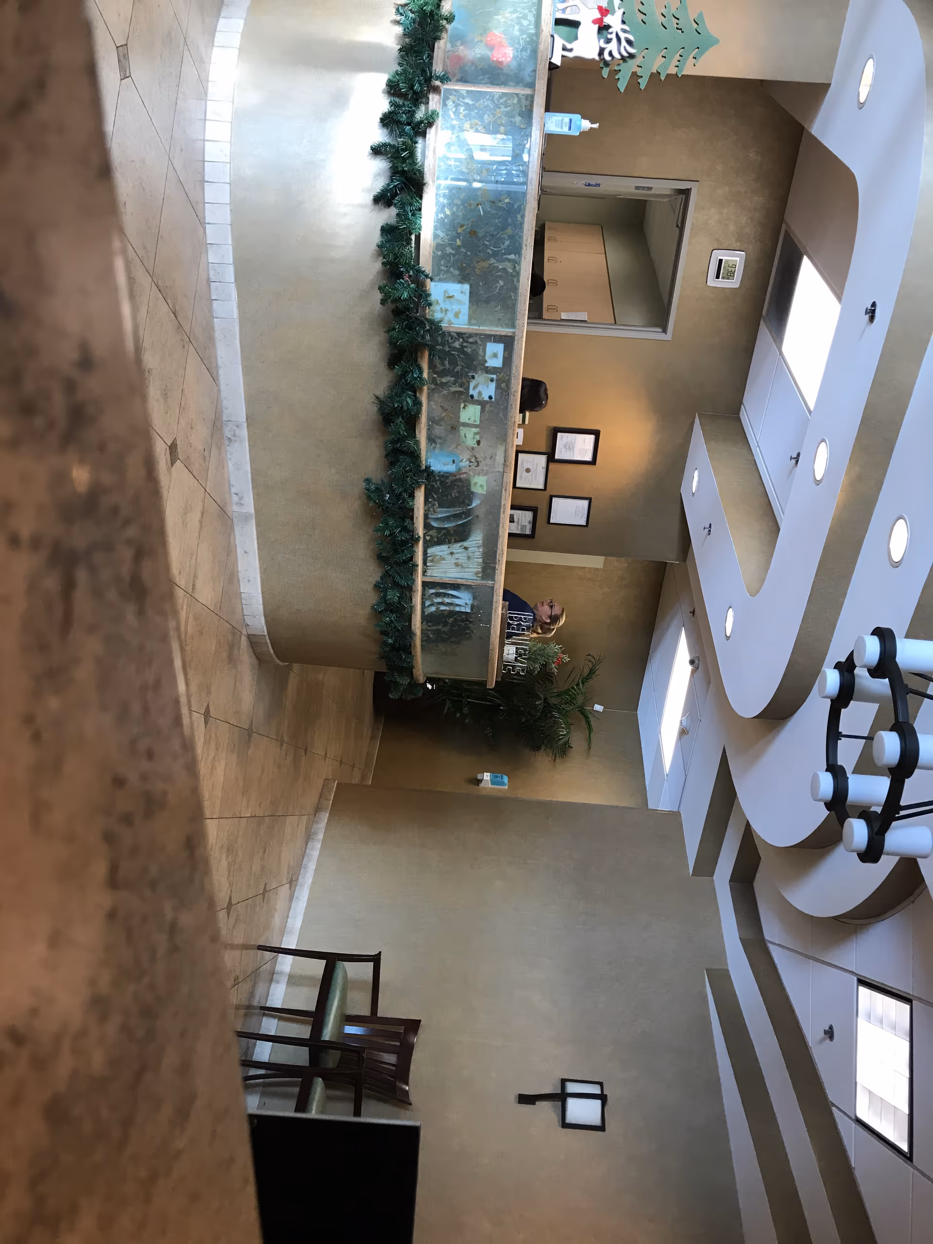 Interior lobby with curved reception desk, green garlands, and framed certificates on the wall.