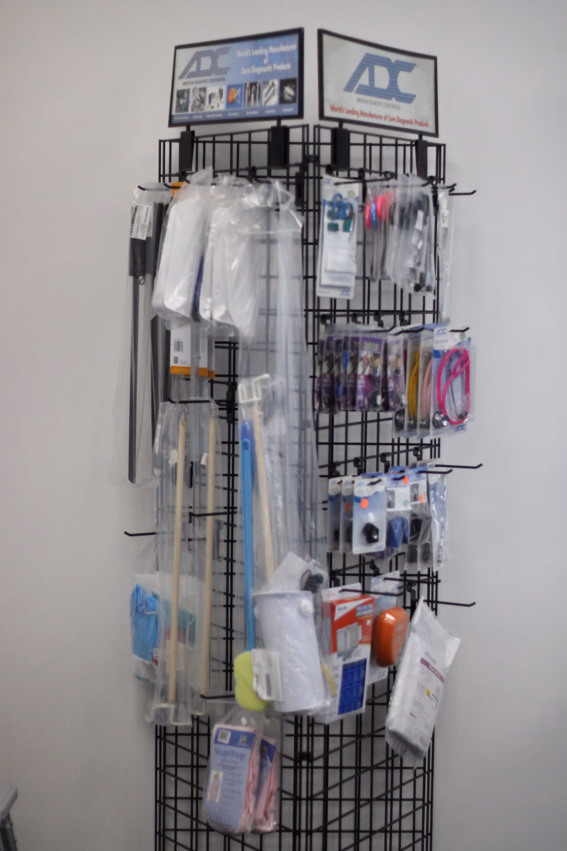 Tall black wire rack filled with packaged medical supplies and accessories against a white wall.