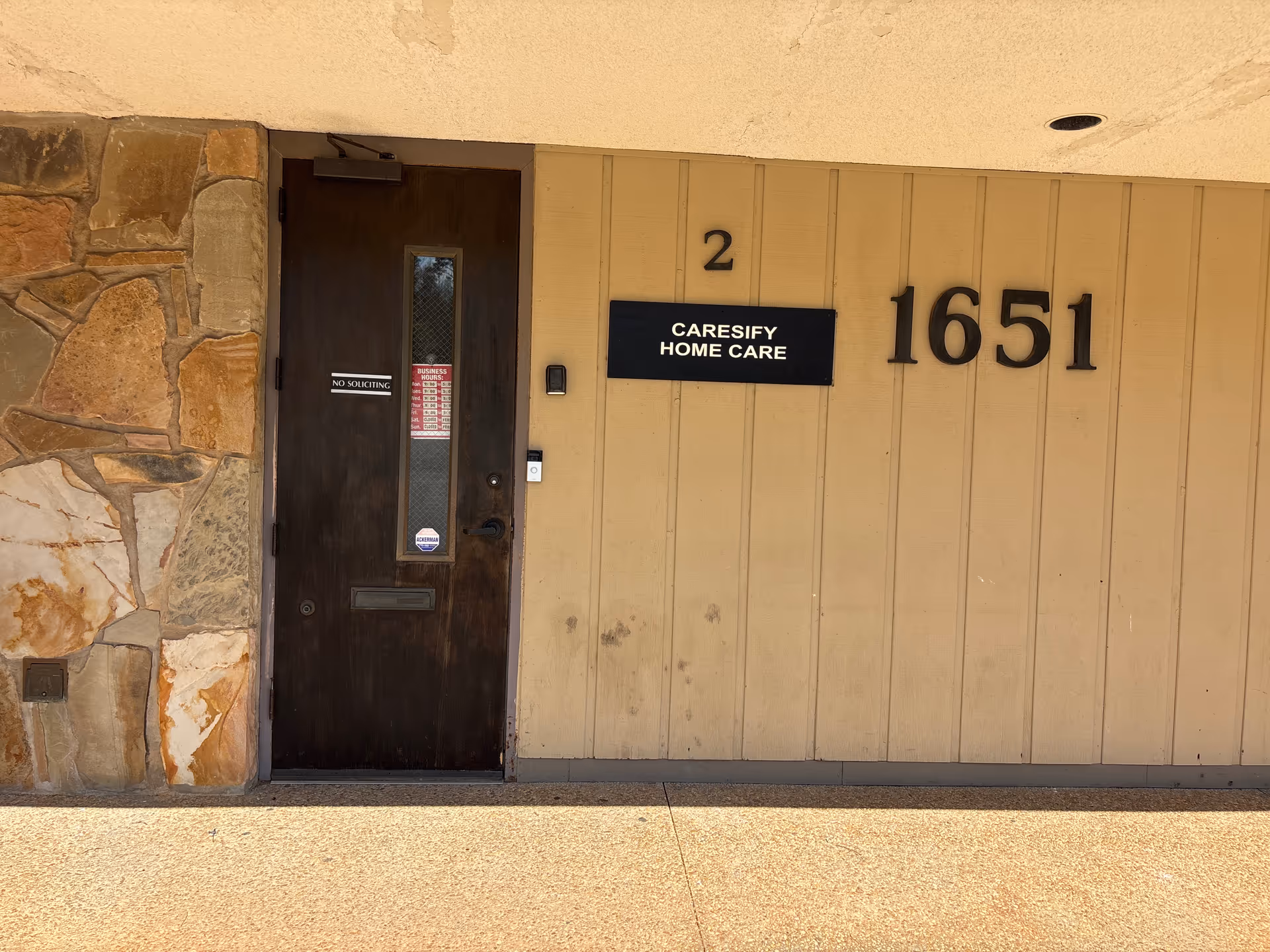 Dark wooden door beside a stone wall and beige exterior with CARESIFY HOME CARE sign.
