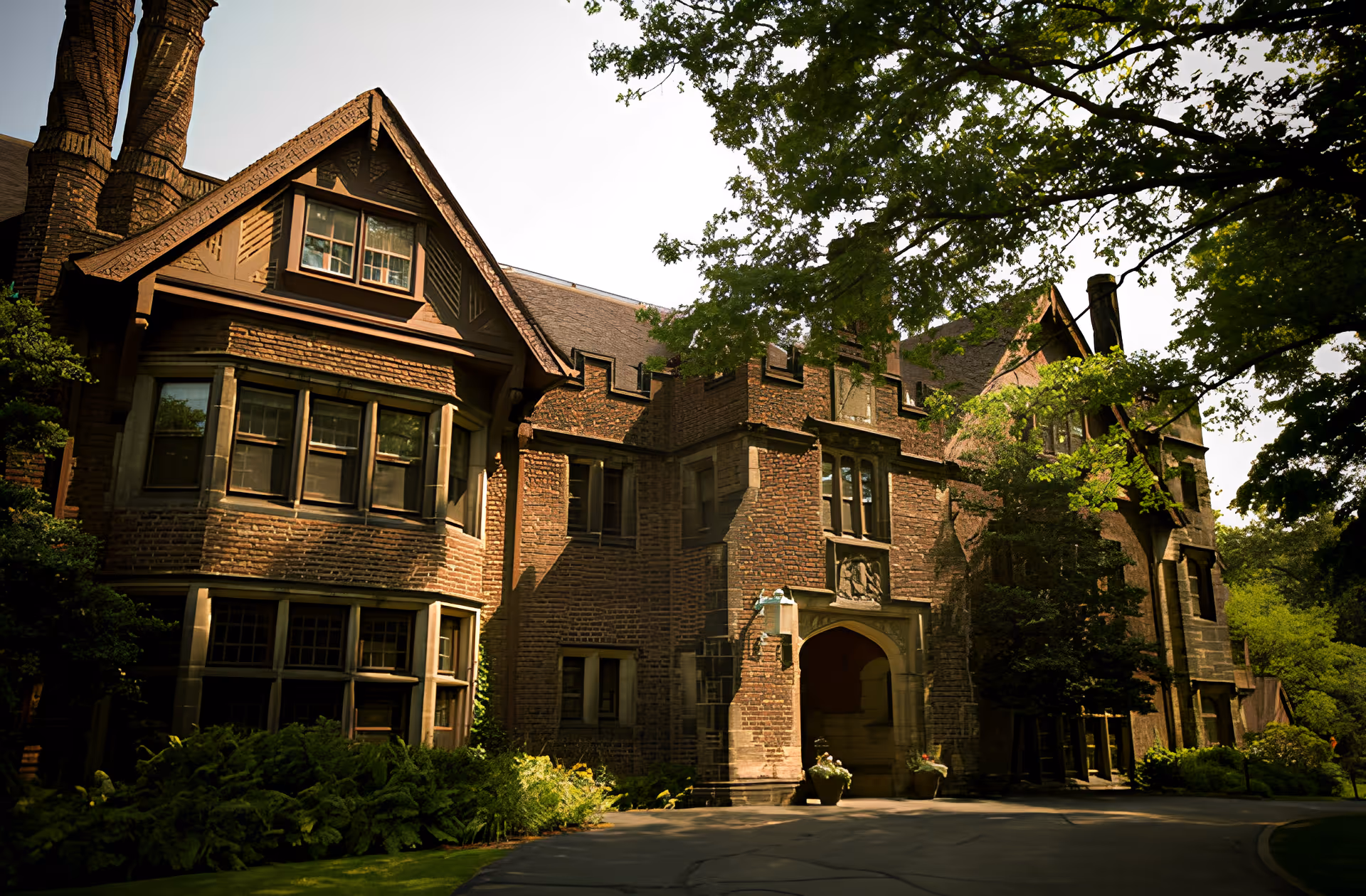 Front exterior of a large brick building with an arched entrance, multiple windows, and surrounding trees and landscaping.