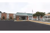 Front view of Charlottesville Health and Rehabilitation Center with entrance, parking lot, and flag.