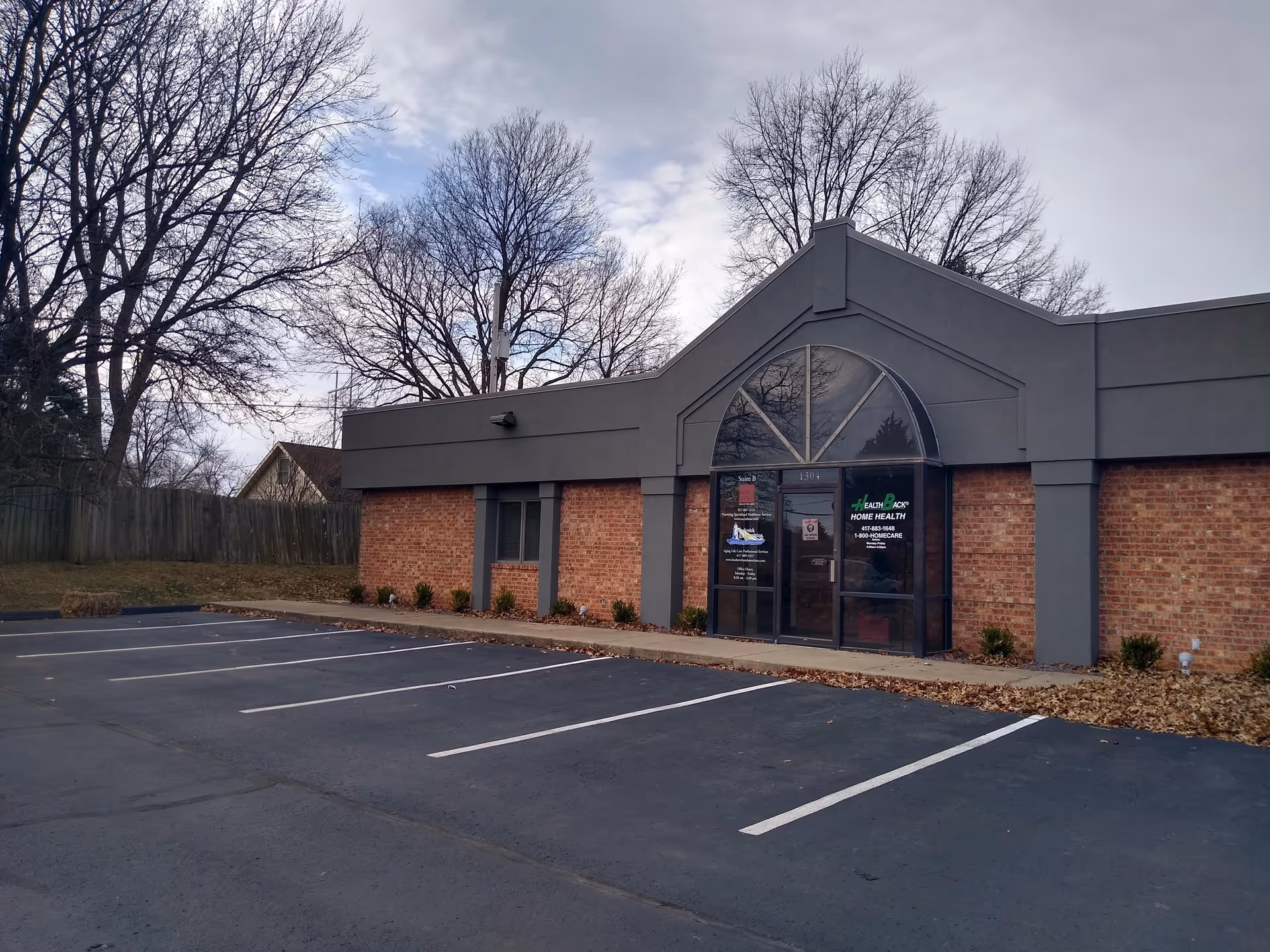 Brick storefront with gray trim and glass doors, Karlovich and Associates sign, and empty parking lot.