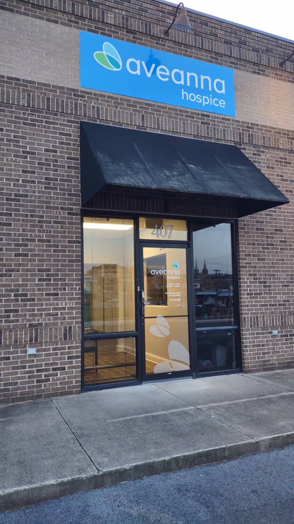 Exterior view of Aveanna Hospice building entrance with blue sign and glass door.