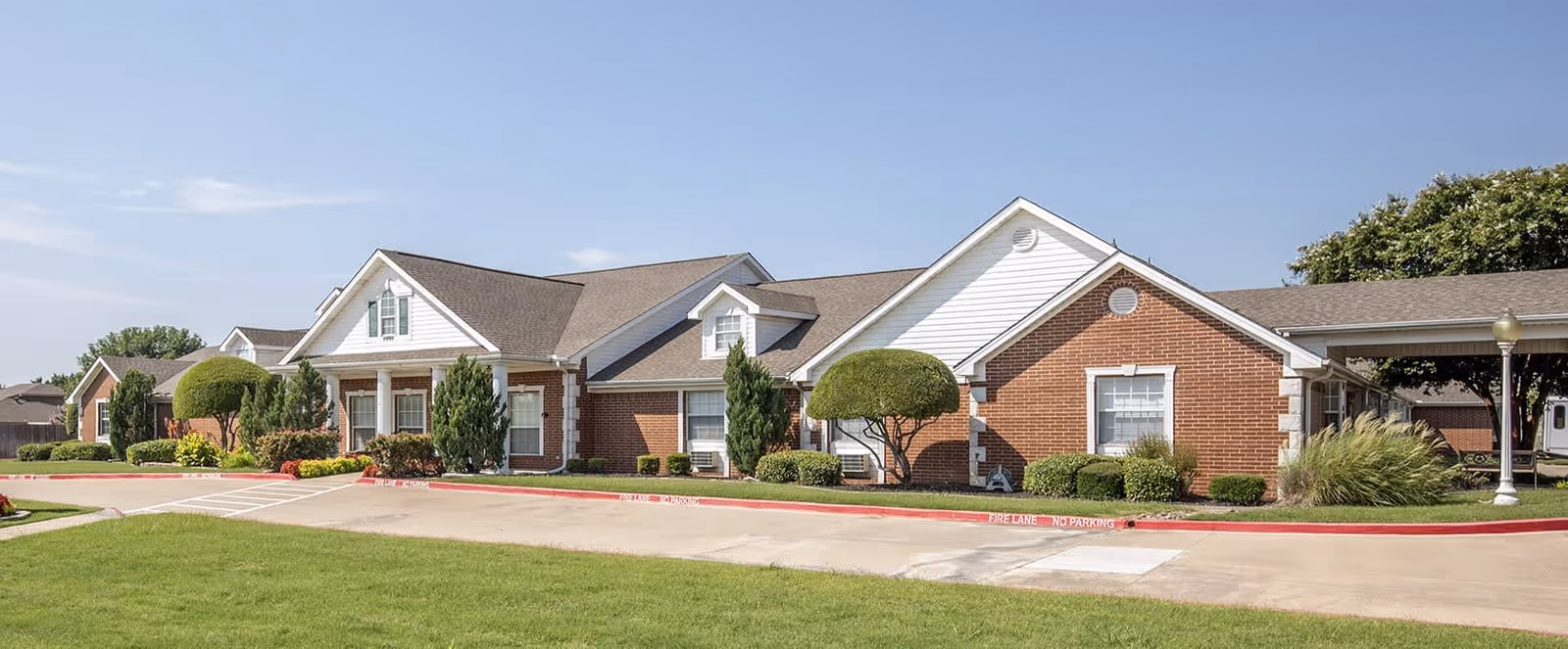 Front exterior of a single-story brick senior living building with a manicured lawn and circular driveway.