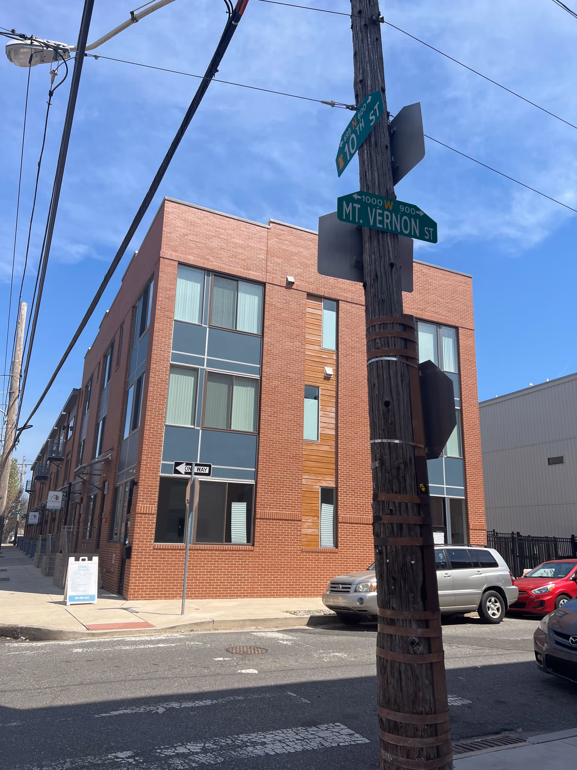 Brick multi-story building on a street corner with signs, power lines, and parked cars.