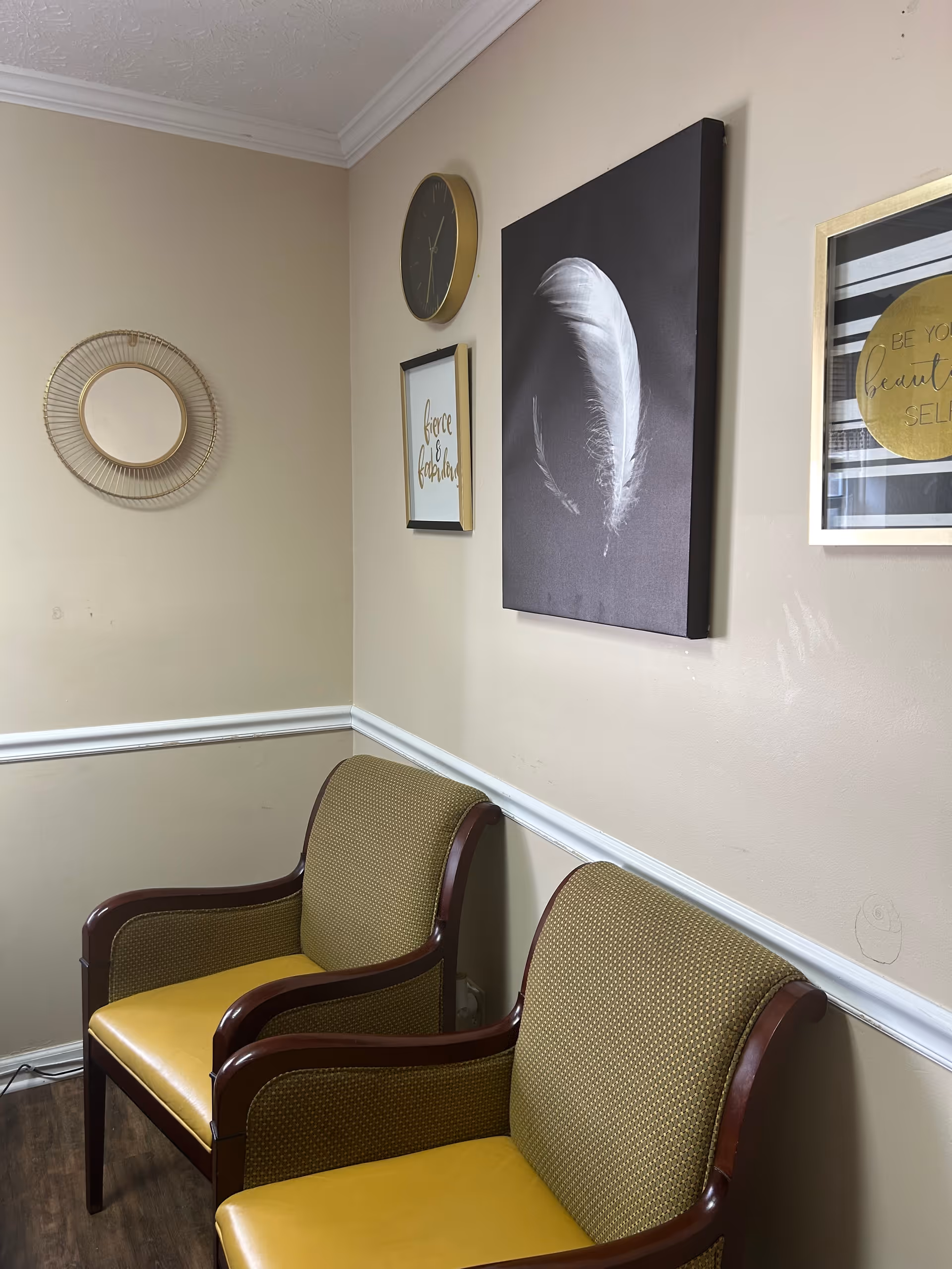 Corner of a beige waiting area with two mustard-yellow chairs and wall art.