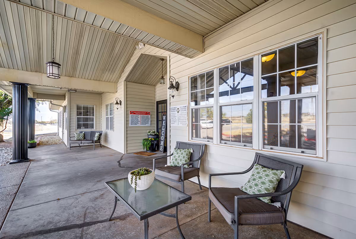 Outdoor seating area with chairs, table, and cushions along a beige facility wall.