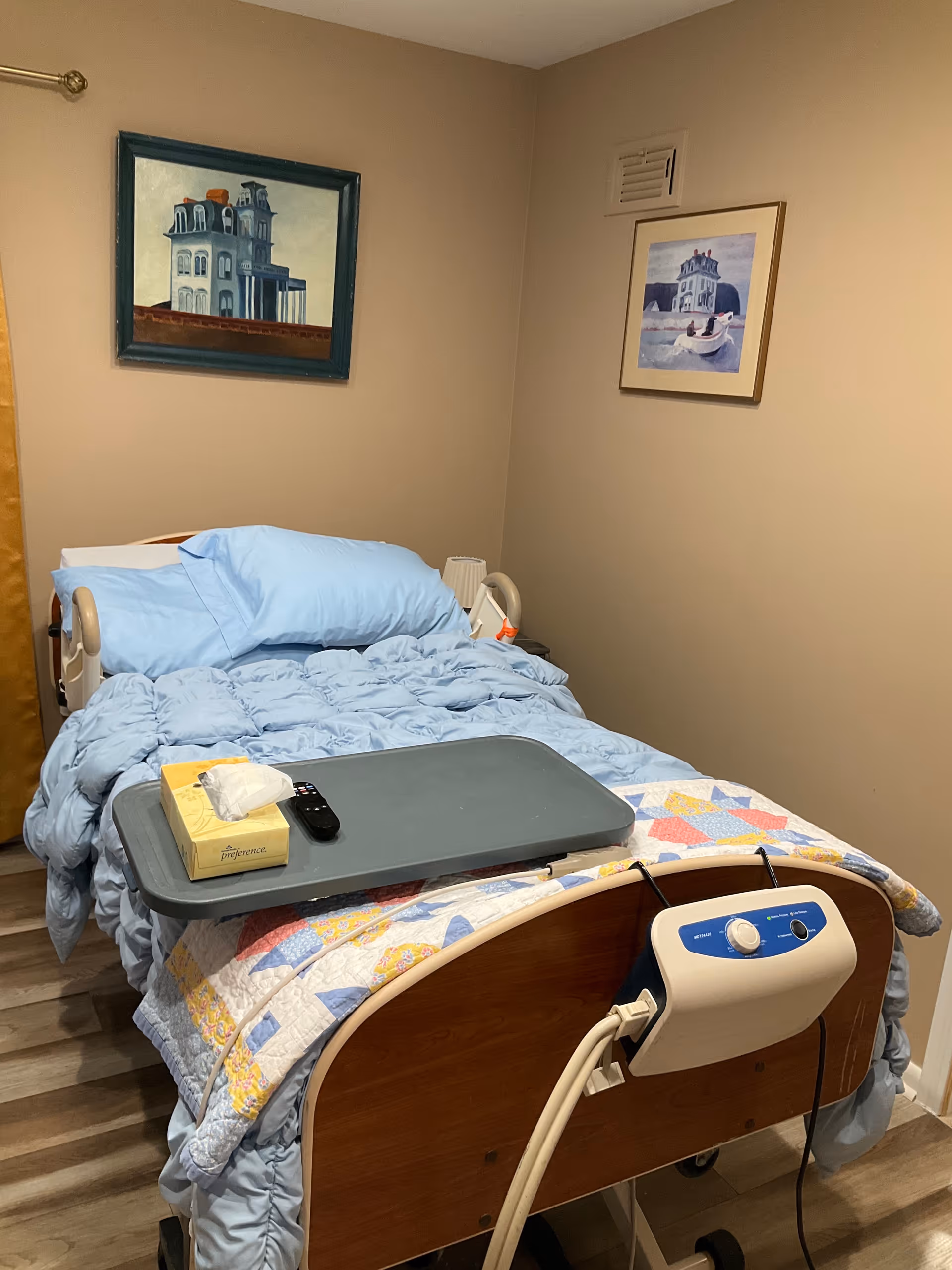 A hospital-style bed with blue bedding sits in a small bedroom.