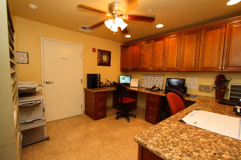 Interior staff workspace with granite counters, wooden cabinets, computers, and office chairs.