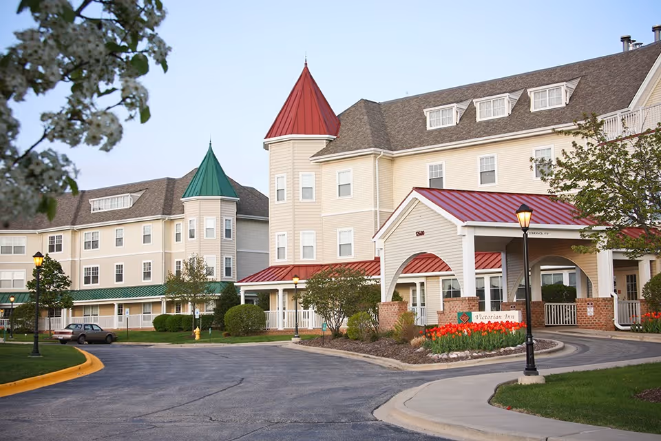 Exterior view of Victorian Village senior living facility with beige walls, red roof, and tower accents.