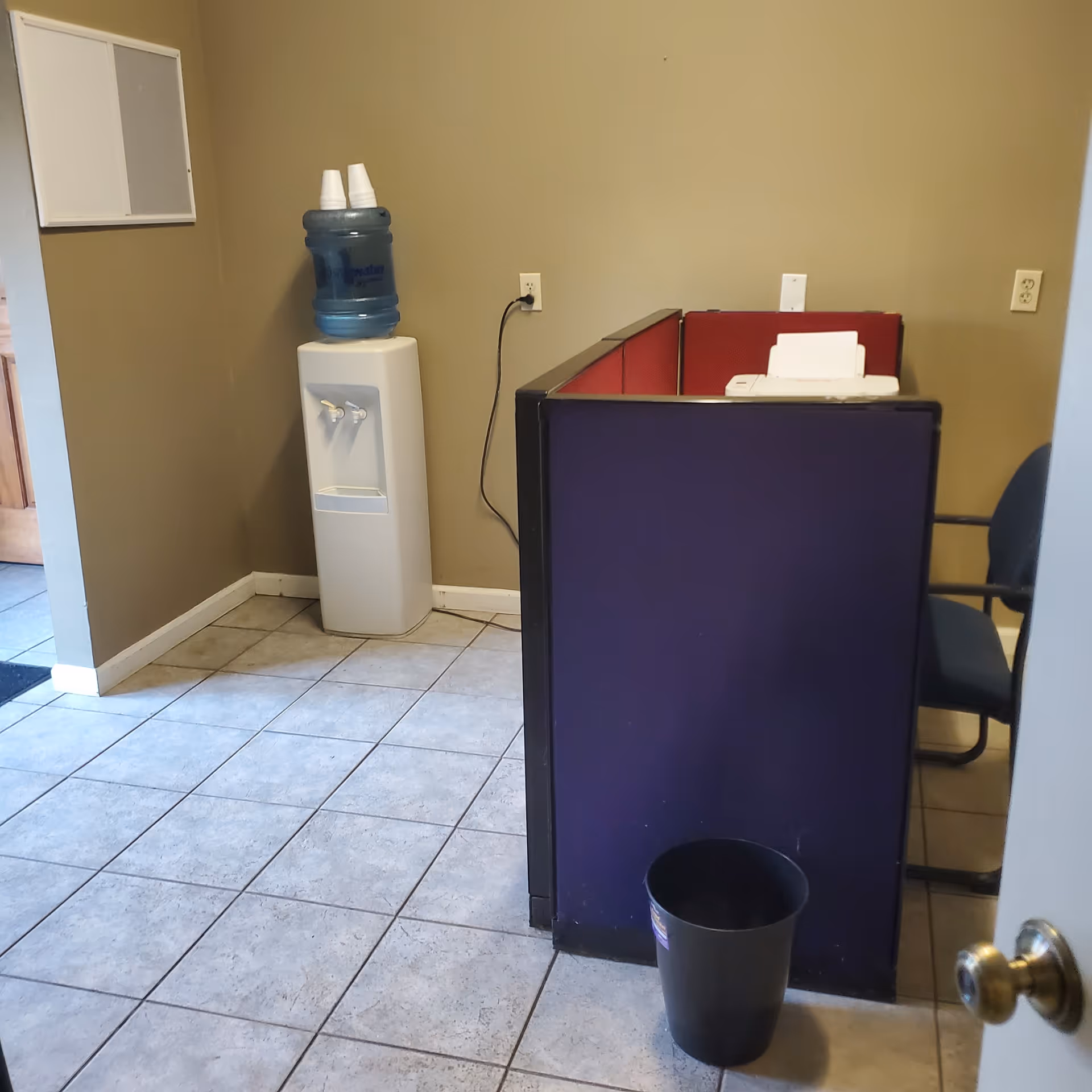 Water cooler beside a purple-front reception desk in a small beige-walled interior.