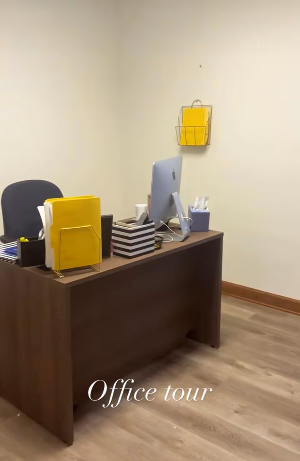 Office desk with computer, yellow folders, and organizers in a small reception area.