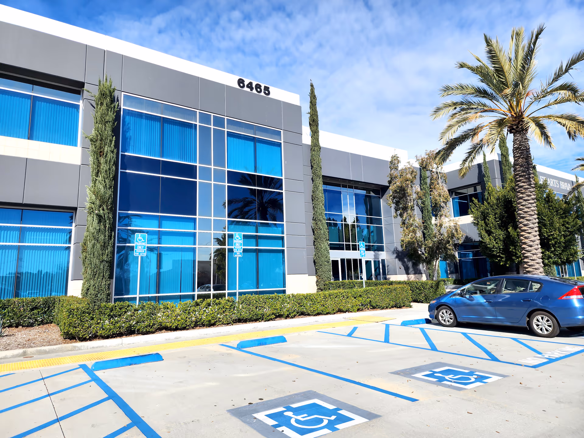 Exterior view of a modern hospice building with blue-tinted windows and a parking lot.