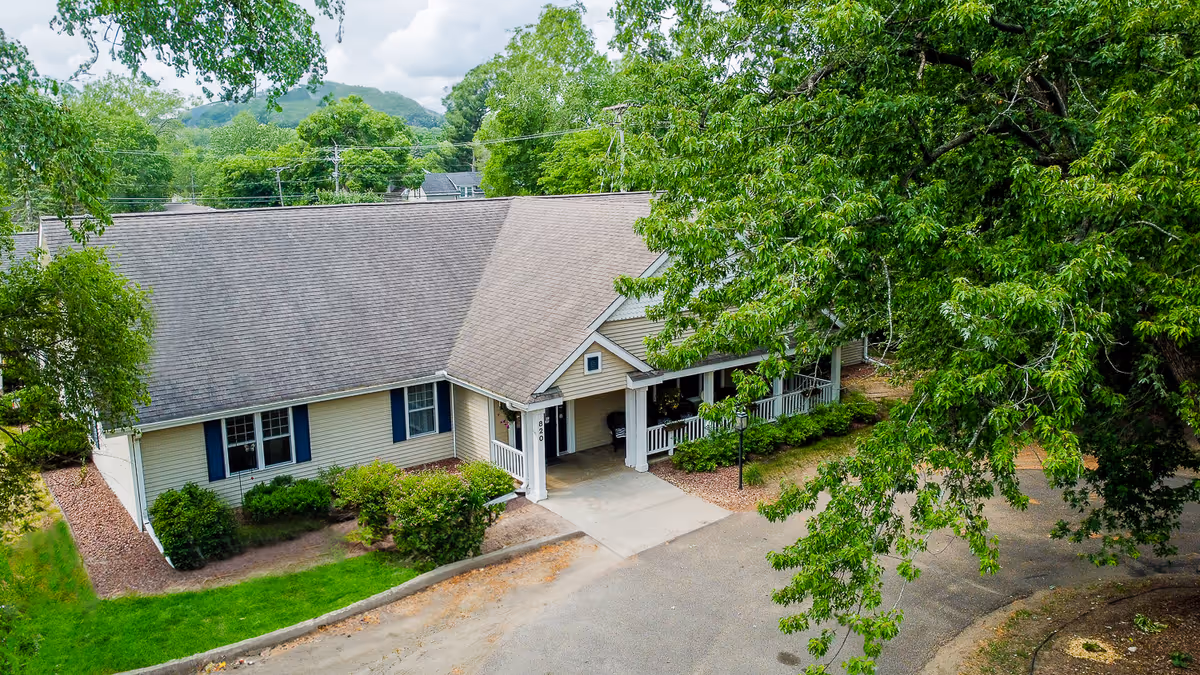 Aerial view of a single-story beige senior living building with a covered entrance, surrounding trees, and a curved driveway.