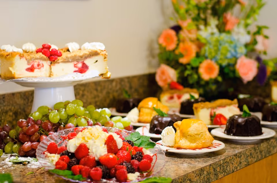Assorted desserts, fruits, and pastries arranged on a counter with flowers in the background