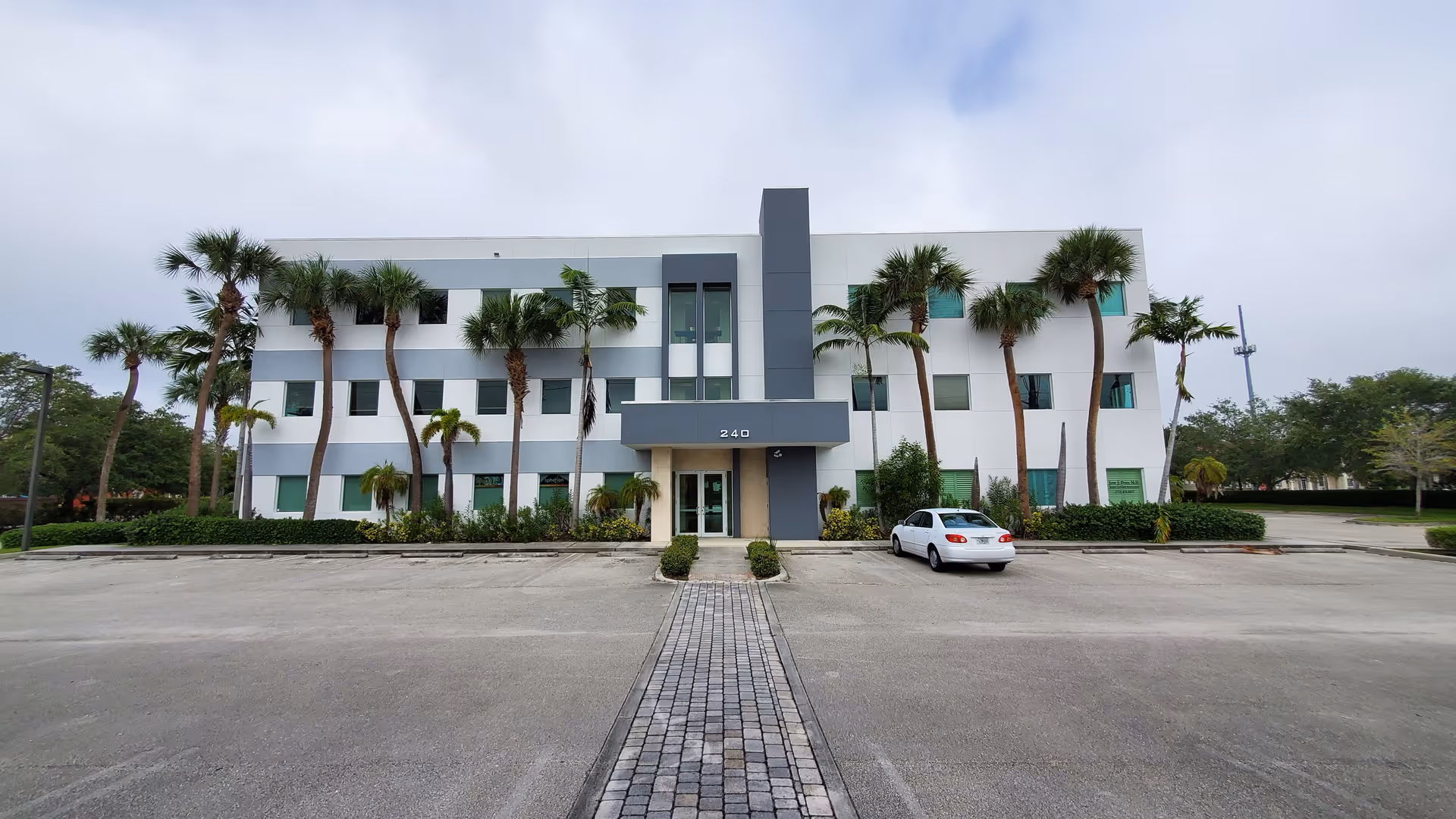 Exterior view of a modern, palm-lined, three-story building with a parking lot.
