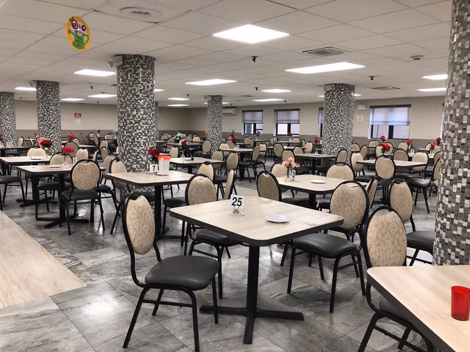 Spacious indoor dining hall in a senior facility with many tables and centerpieces.