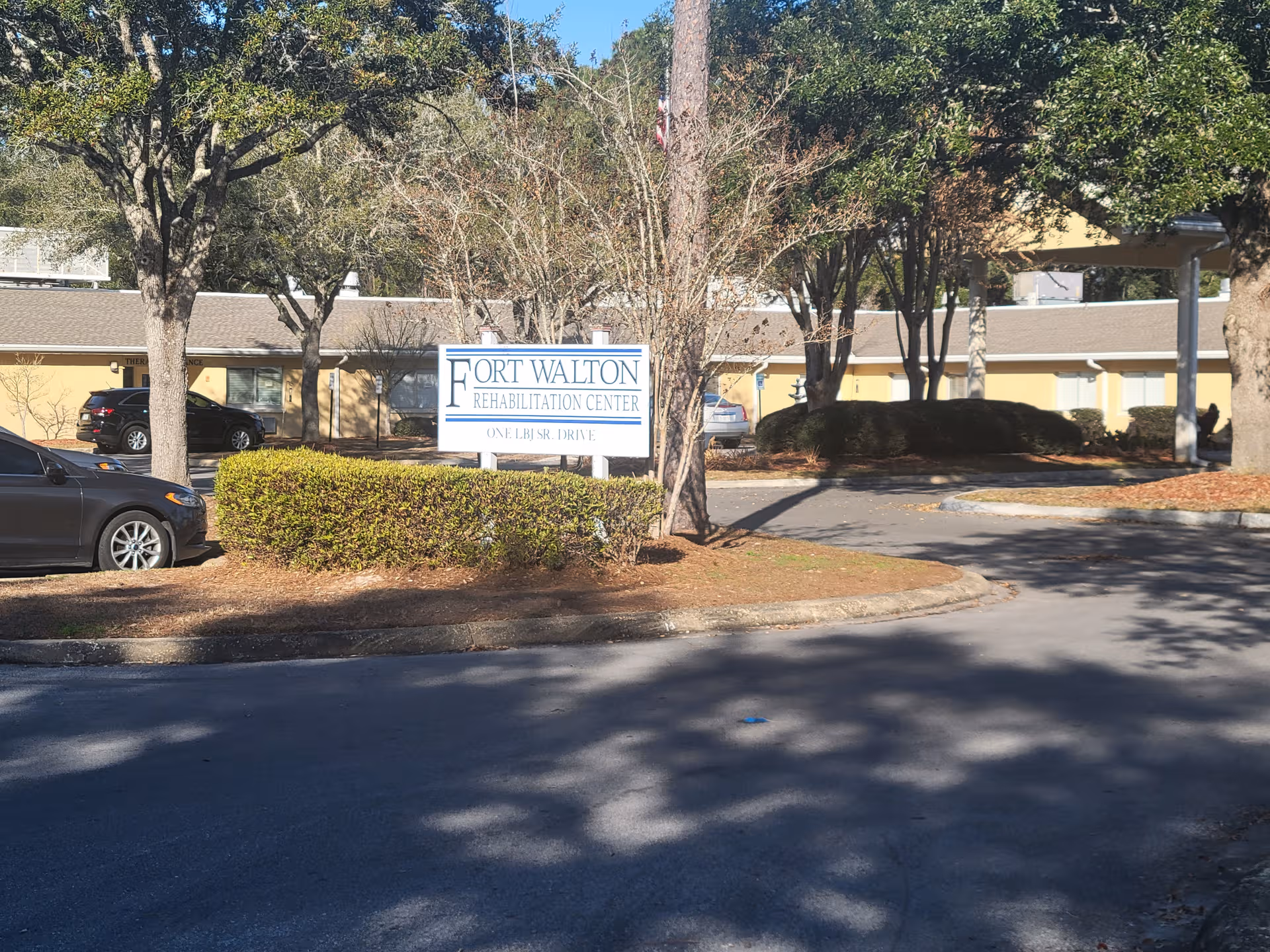 Exterior view of Fort Walton Rehabilitation Center with sign, trees, and parking.