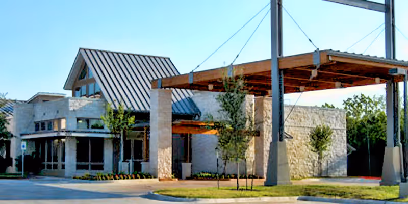 Exterior view of a senior living facility entrance with stone columns and a covered porte-cochère.