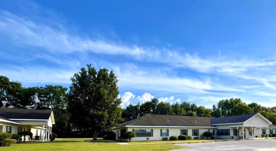Exterior view of a single-story senior living facility with lawn and trees.