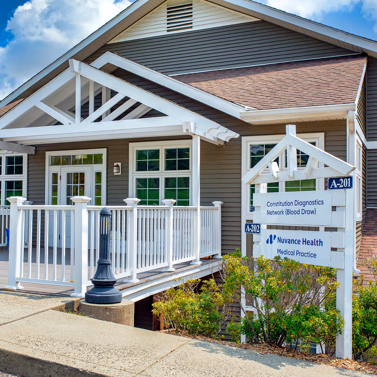 Exterior view of a clinic with a white railing and signage on tan siding.