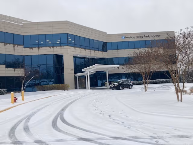 Snow-covered parking area in front of a glass-front medical office building.