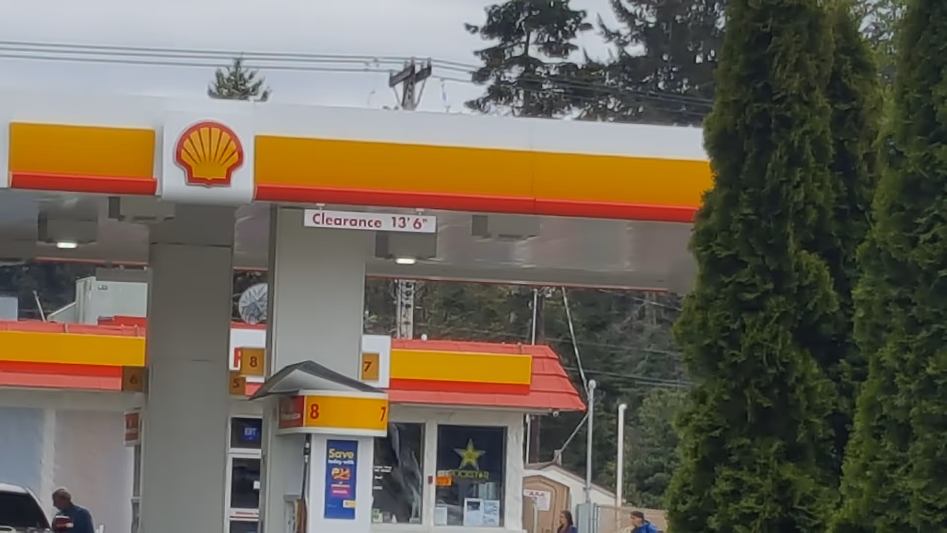 Shell gas station exterior with pumps under a yellow-red canopy and clearance sign.