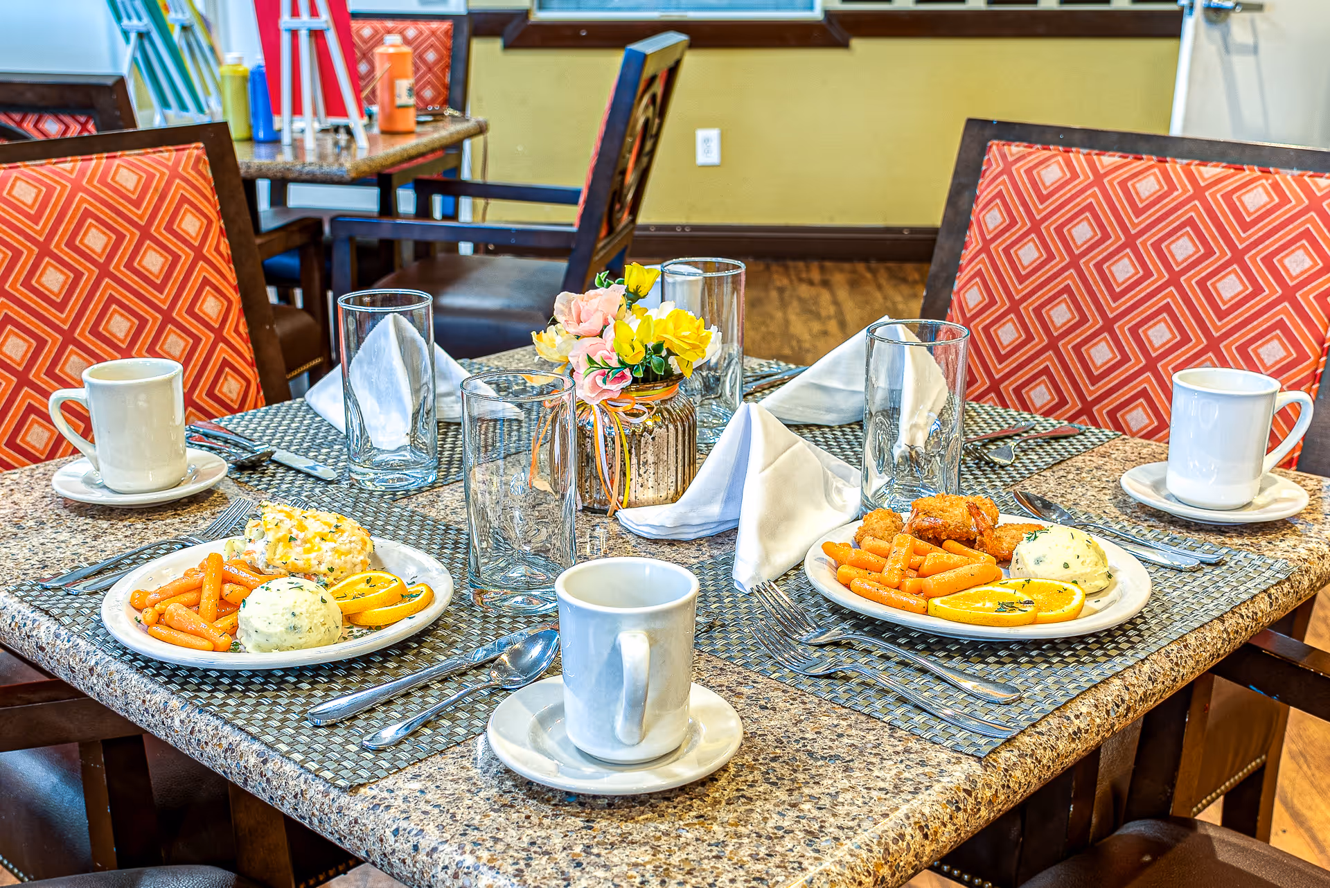 A polished dining table set with plates, mugs, napkins, and a floral centerpiece.