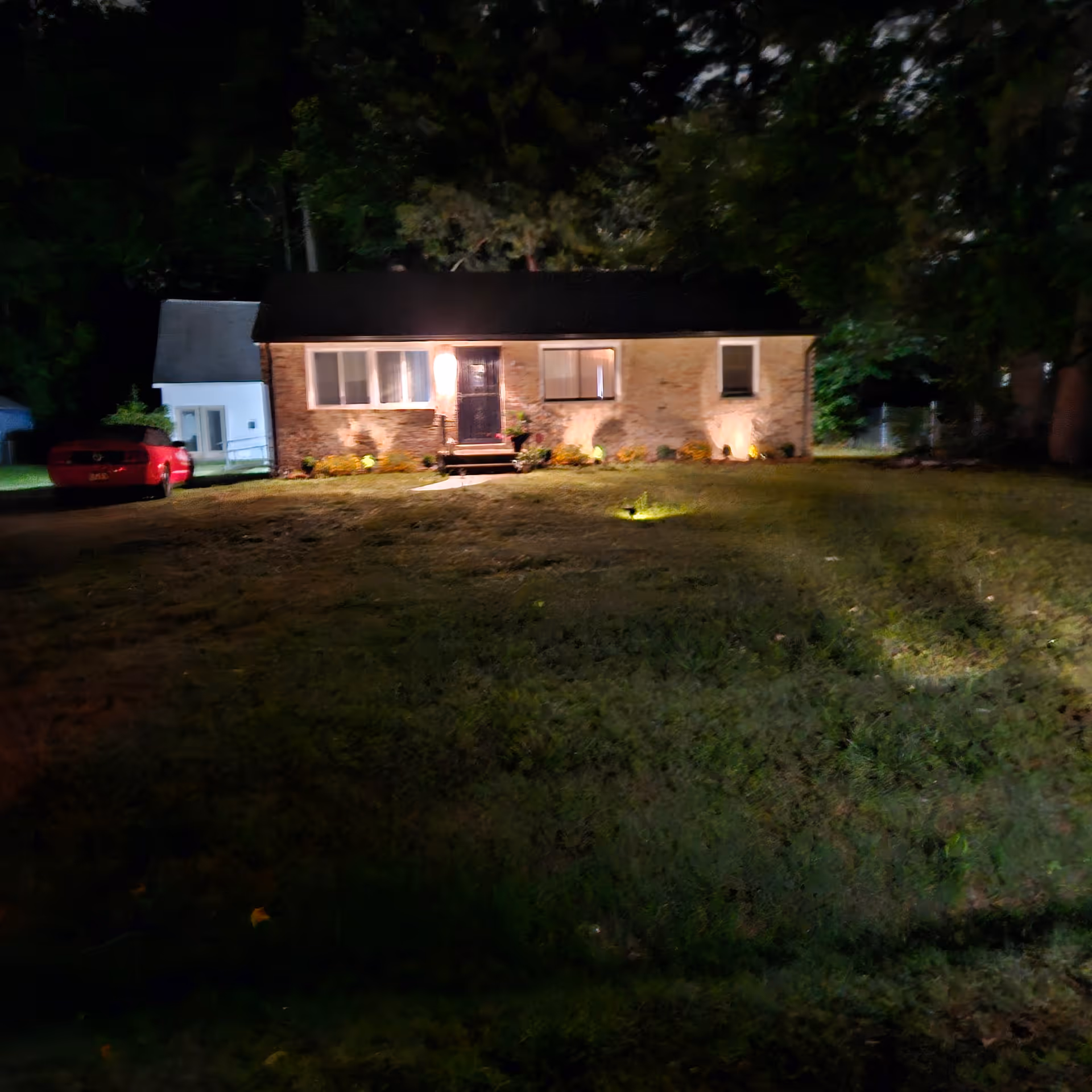 Nighttime exterior of brick single-story building with front steps and garden lighting.
